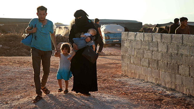 جابر كروان يسير مع زوجته ولاء وهم يحملون طفليهما في مخيم للنازحين السوريين في عتمة
